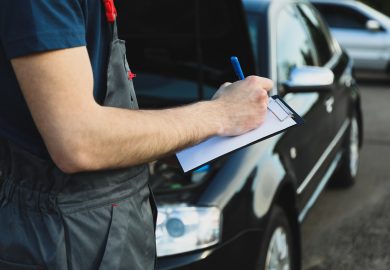 A man in overalls writes to a clipboard. Mechanic. Car inspection